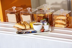 A breakfast buffet with various breads, pastries, and beverages in clear containers. - Première Classe Paris Ouest - Gennevilliers Barbanniers (Gennevilliers)