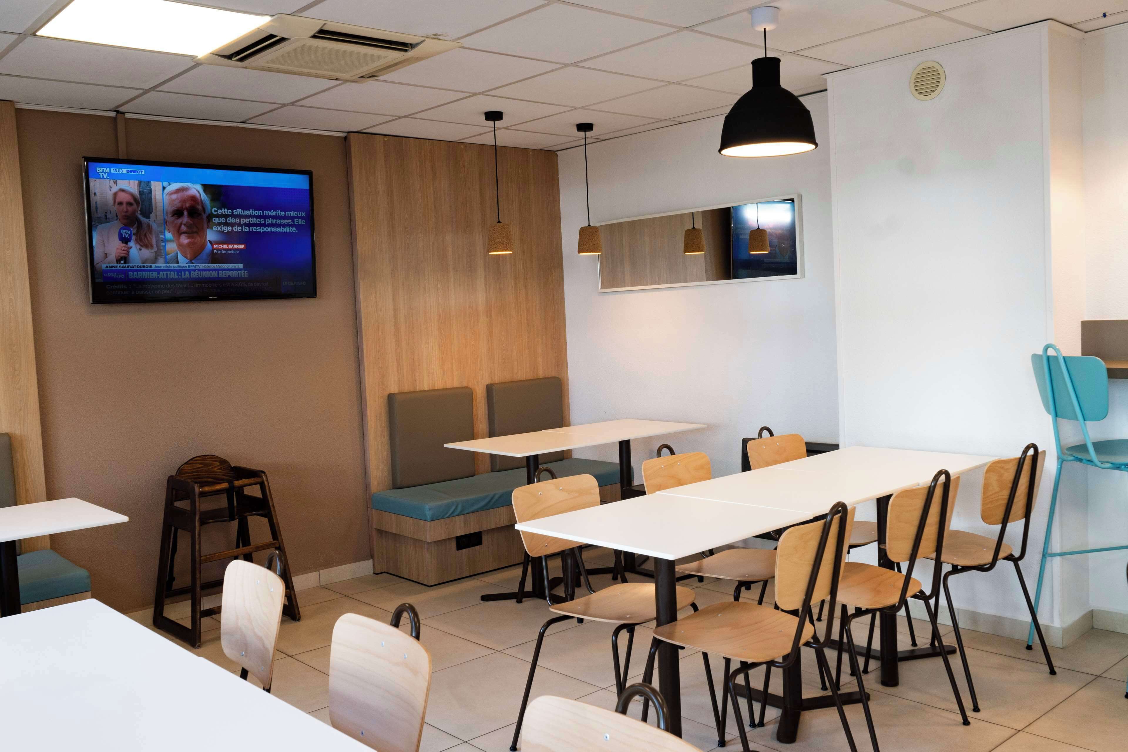 Un comedor moderno con mesas, sillas y un televisor que muestra un noticiero.