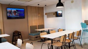 Un comedor moderno con mesas, sillas y un televisor que muestra un noticiero.
