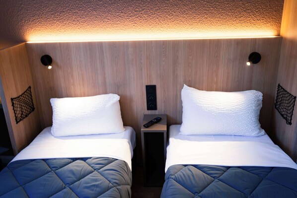 A hotel room with two beds, a small bedside table with a remote control, and a wall-mounted light fixture. - Première Classe Paris Ouest - Gennevilliers Barbanniers (Gennevilliers)