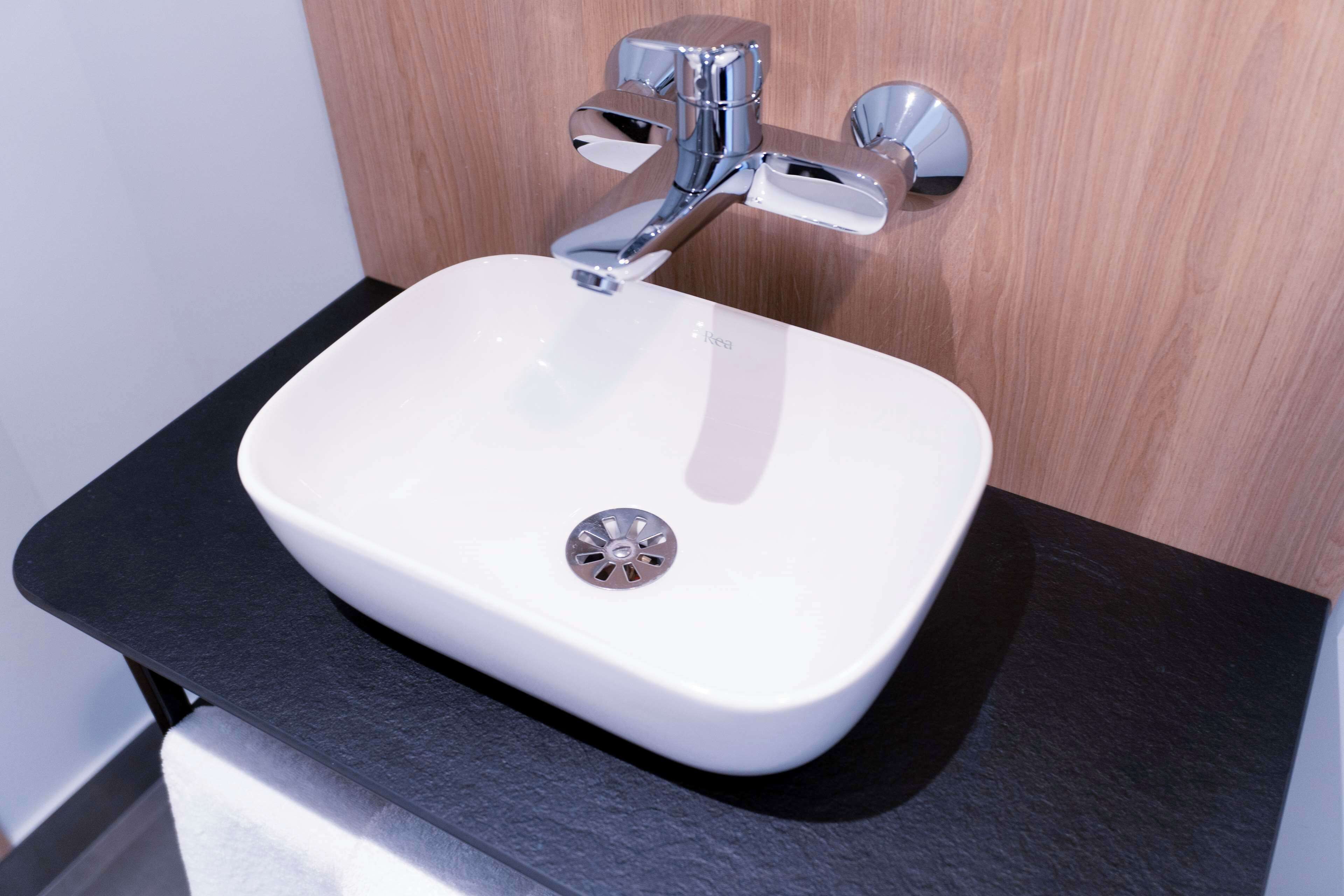 Un évier blanc avec un robinet chromé, installé sur un plan de travail noir, le tout adossé à un mur en bois.
