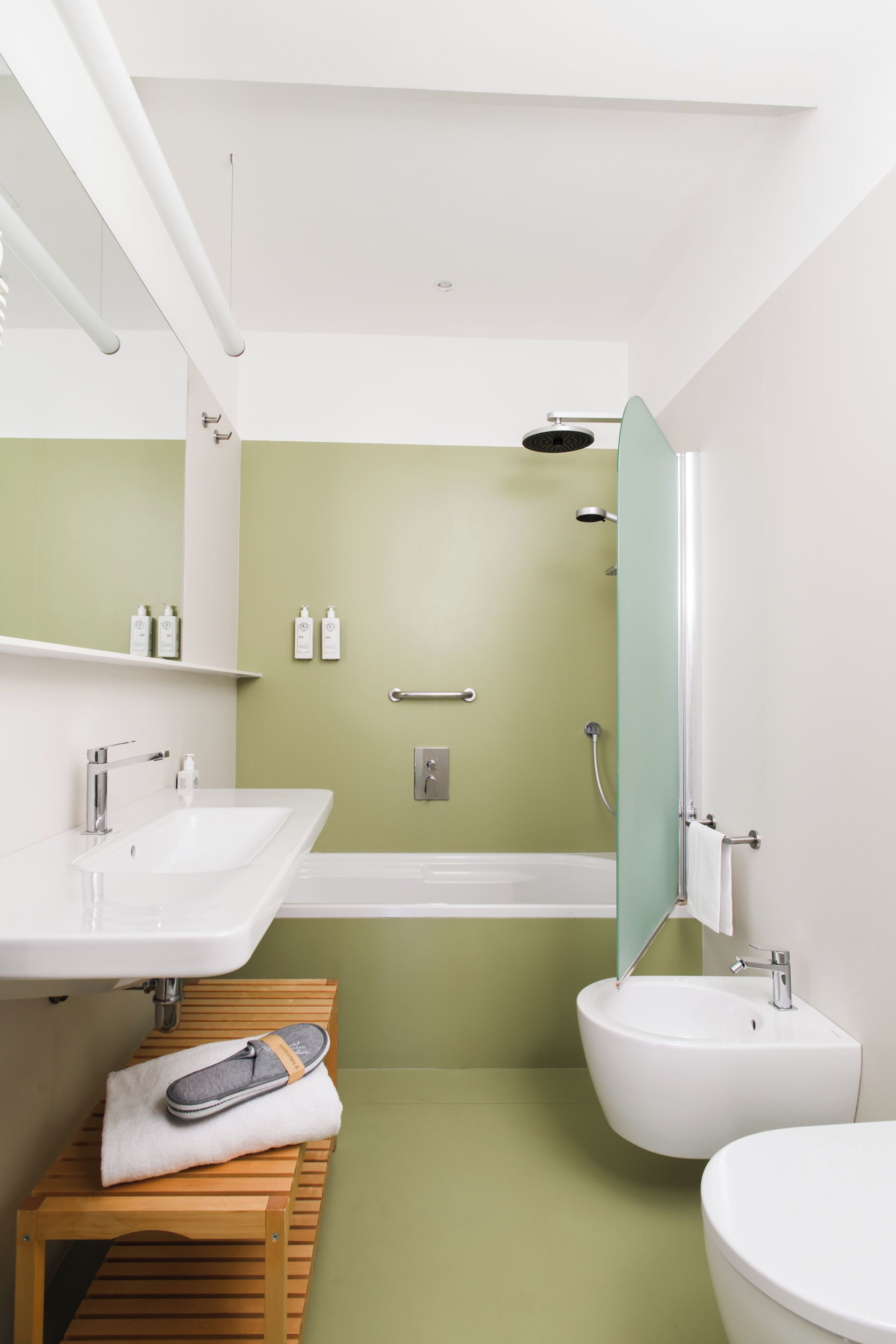 Un baño moderno con un lavamanos blanco, un taburete de madera, un bidé y una zona de ducha.