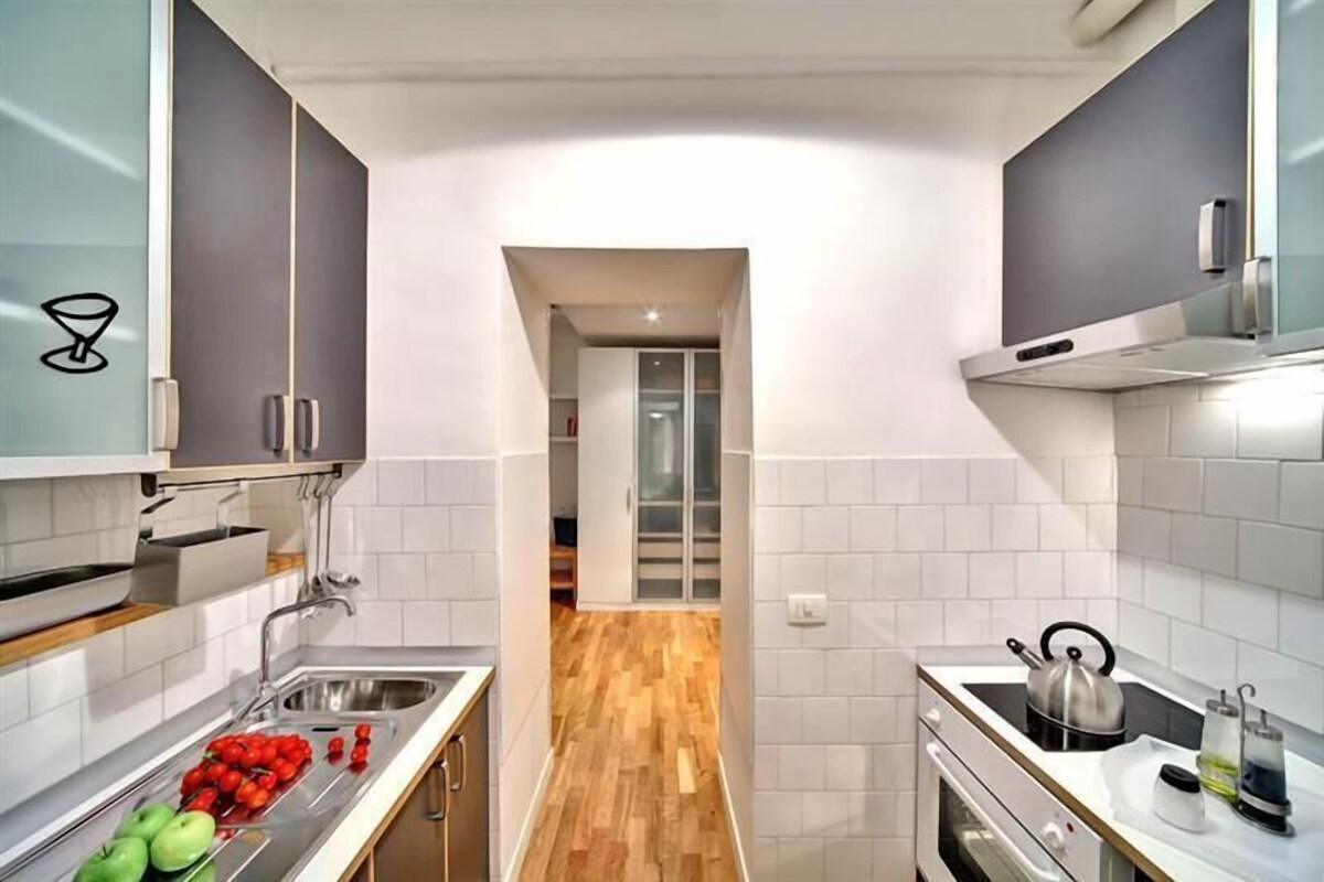 A modern kitchen with white tiles, a wooden floor, and stainless steel appliances.