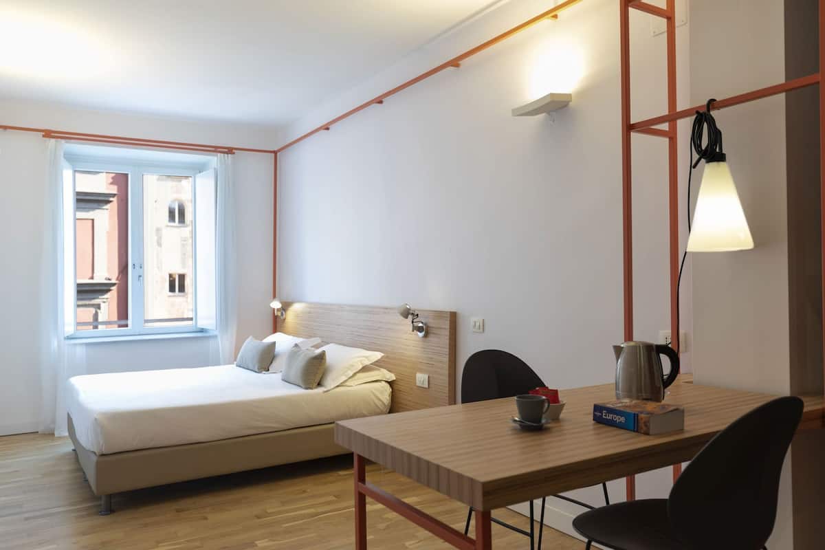 A bedroom with a bed, a wooden table with chairs, a coffee maker, and a lamp.
