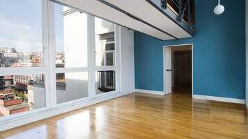 Una habitación amplia con ventanas grandes, piso de madera y una escalera que sube a un nivel superior.