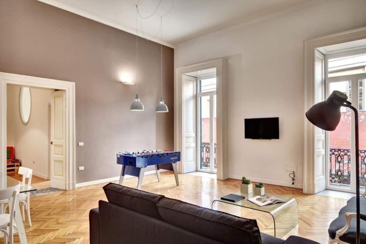 A spacious living room with a foosball table, a sofa, a coffee table, and a TV mounted on the wall.
