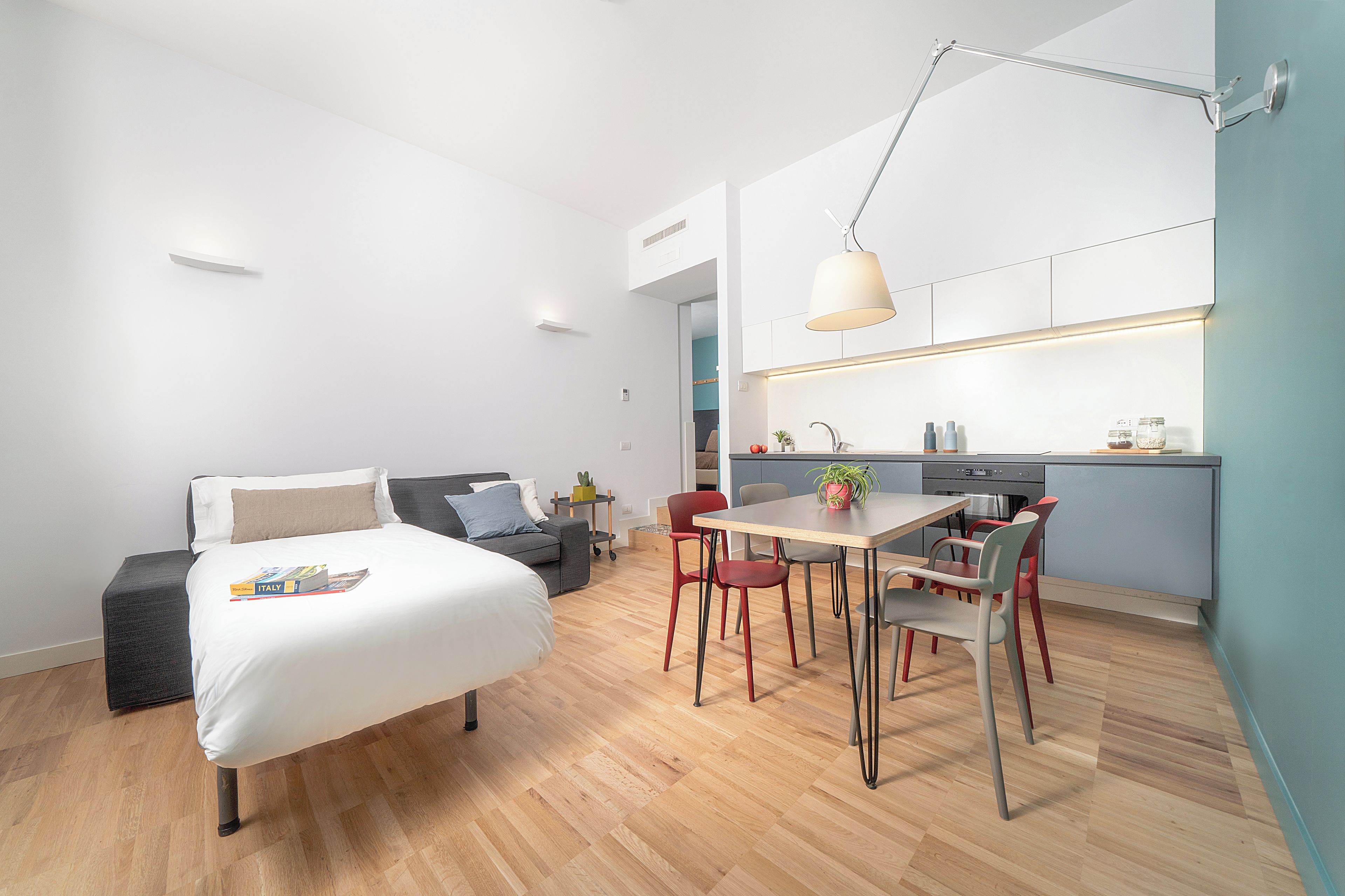 Un espace de vie moderne et compact comprenant un lit, un coin repas avec des chaises, une cuisine et un petit coin salon.