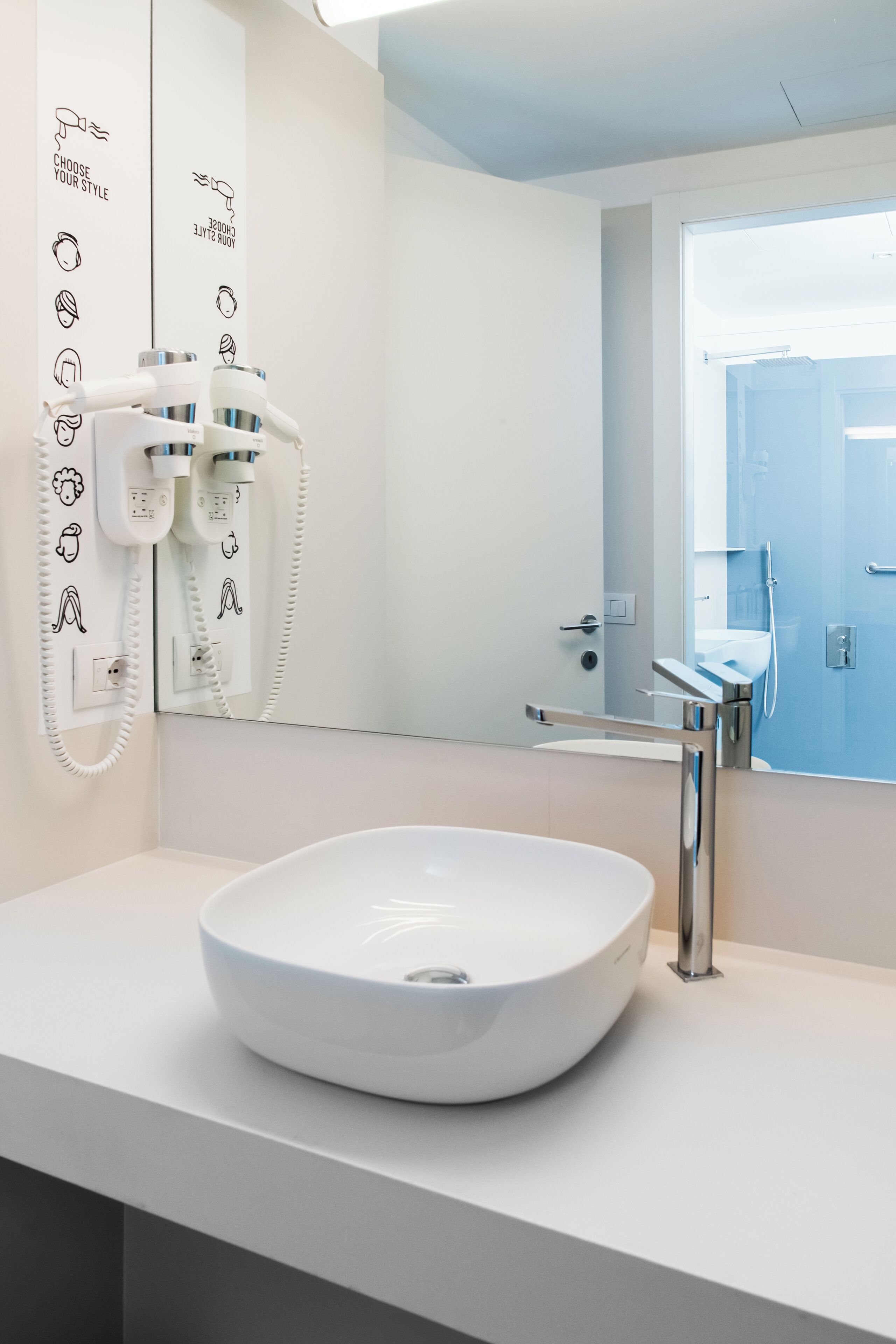 A modern bathroom with a white sink, a hairdryer, and a mirror.