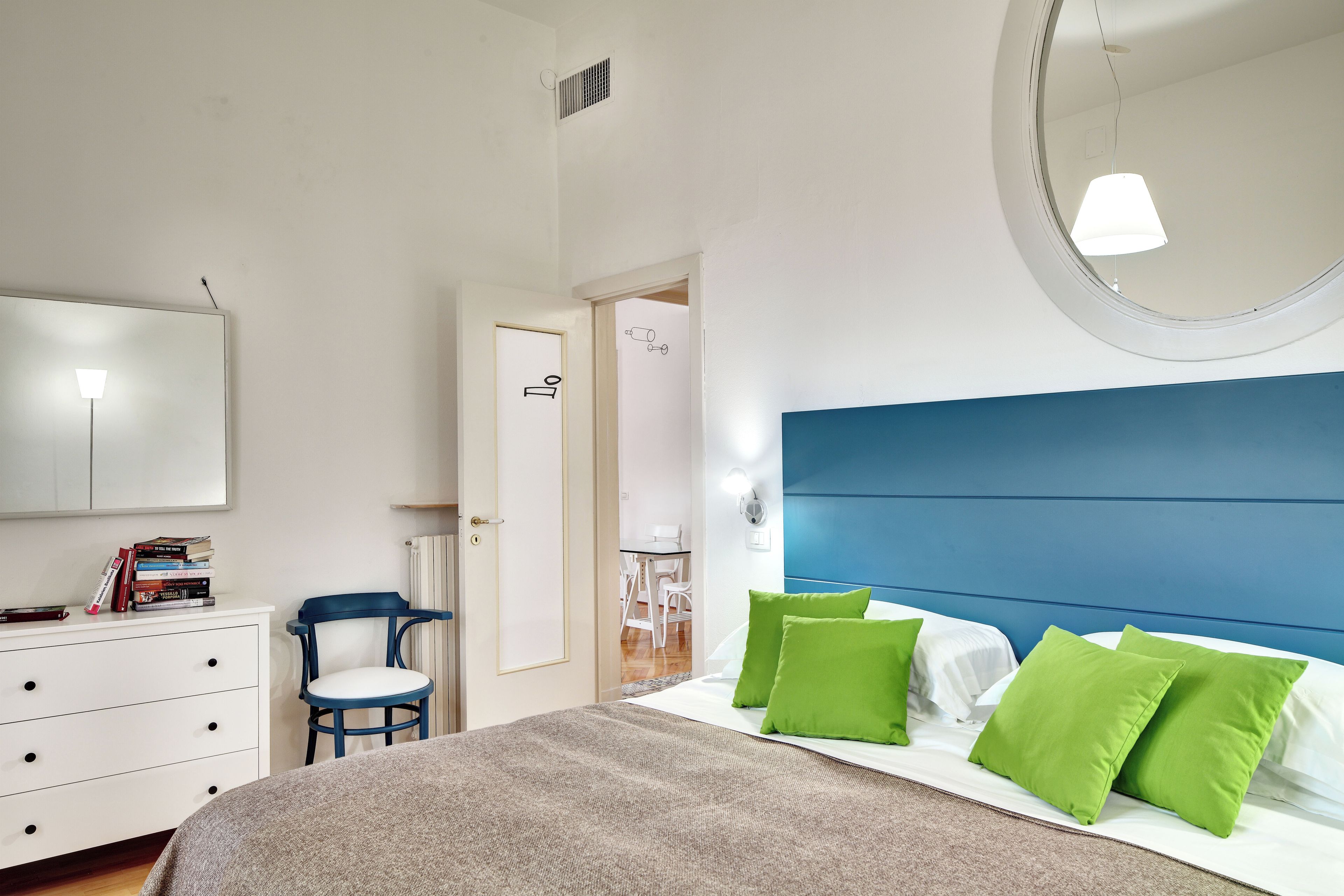 A bedroom with a bed, a dresser, a chair, a mirror, and a door leading to a bathroom.