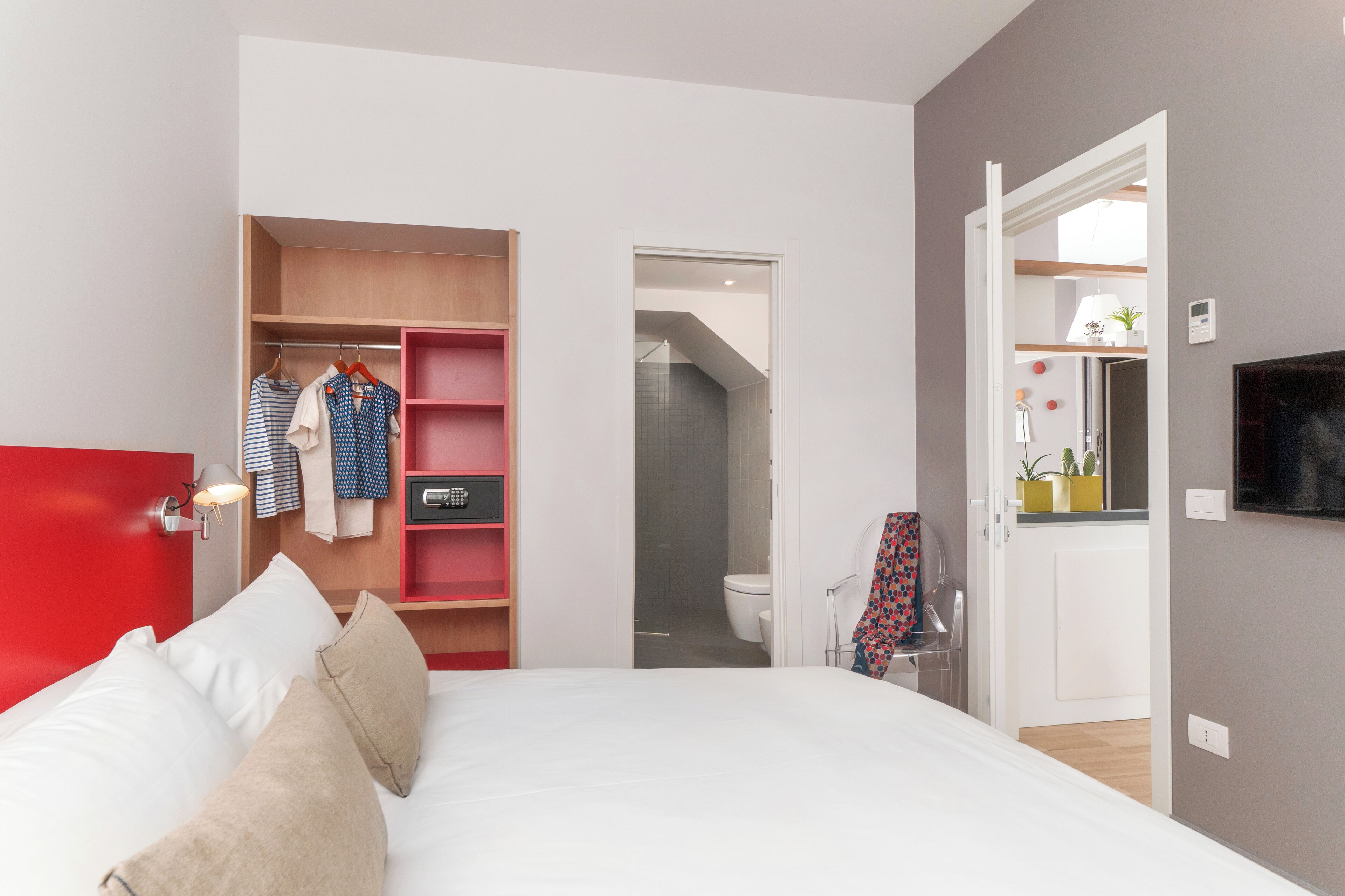 Un dormitorio con cama, armario y baño a la vista, tras una puerta abierta.