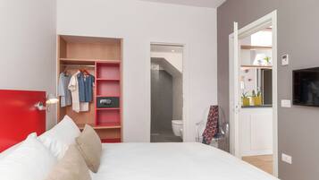 Un dormitorio con cama, armario y baño a la vista, tras una puerta abierta.