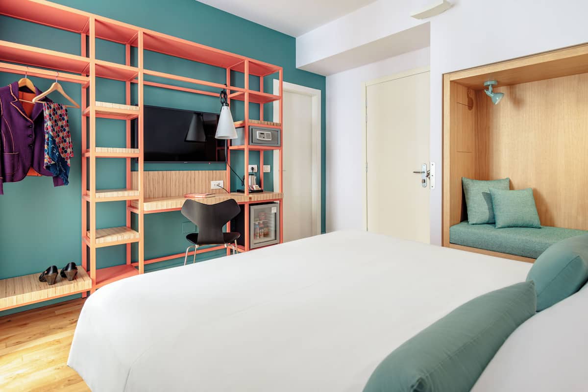 A bedroom with a bed, a desk with a chair, a TV, and a wardrobe.