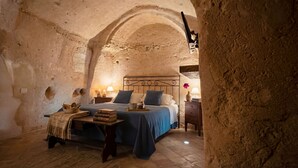 Une chambre rustique avec un lit, une table sur laquelle sont posés des livres et un plateau, et une table de chevet avec une lampe.