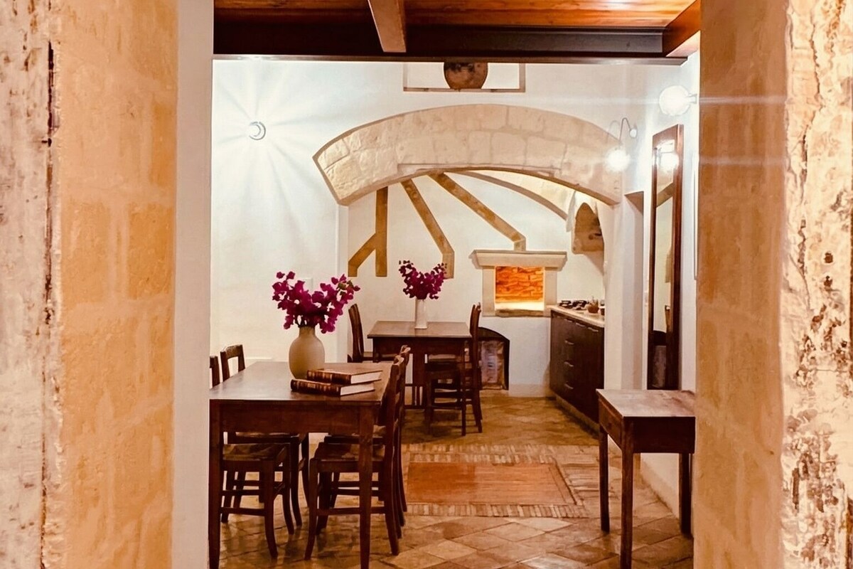 Un coin repas rustique agrémenté d’une arche en pierre, de poutres en bois au plafond et d’un sol carrelé.
