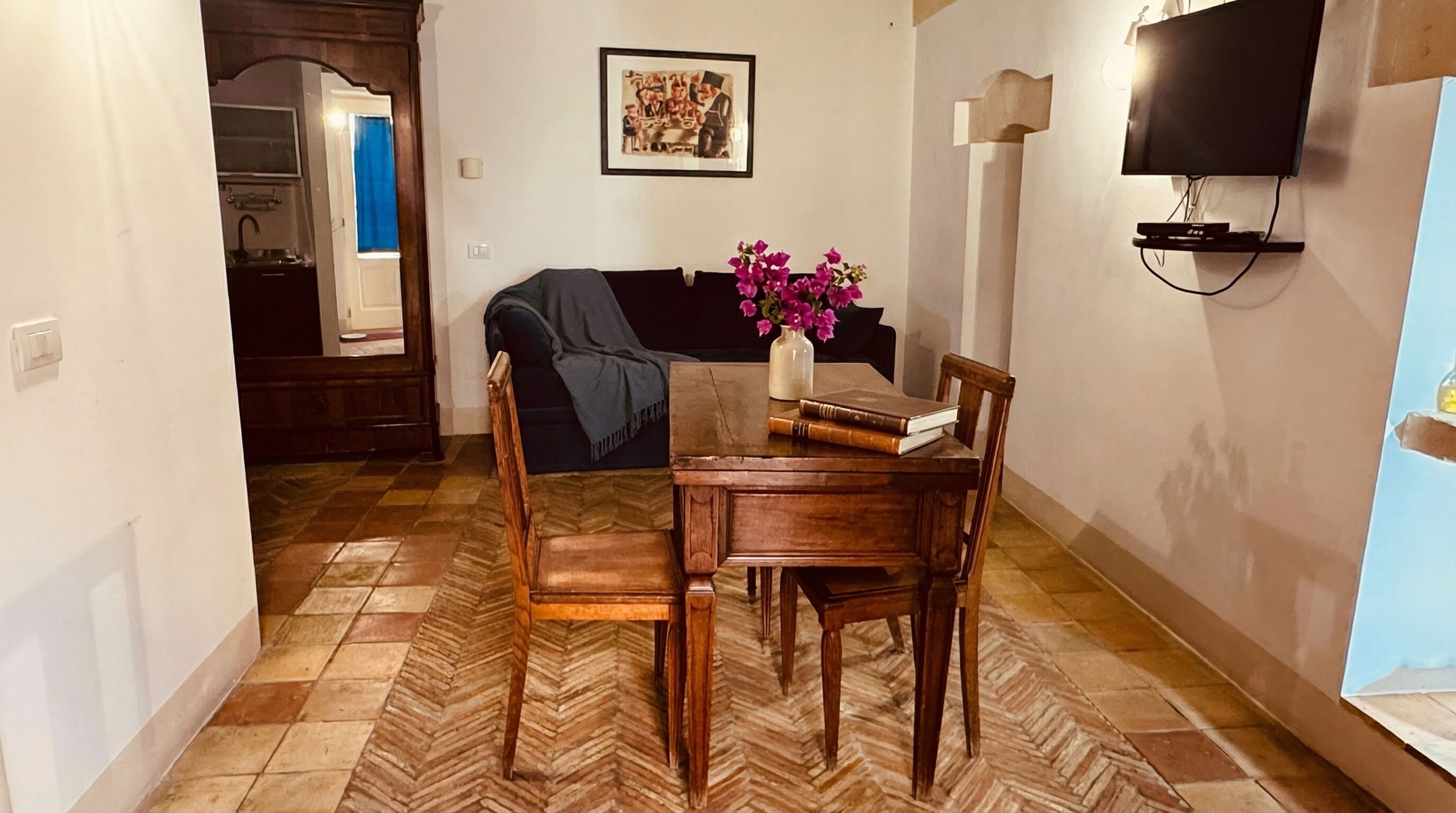 A dining area with a wooden table and chairs, a vase with flowers, and a framed picture on the wall.