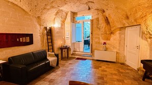 Un intérieur chaleureux avec un mur en pierre, un canapé en cuir noir, une échelle en bois et une porte donnant sur un espace extérieur.