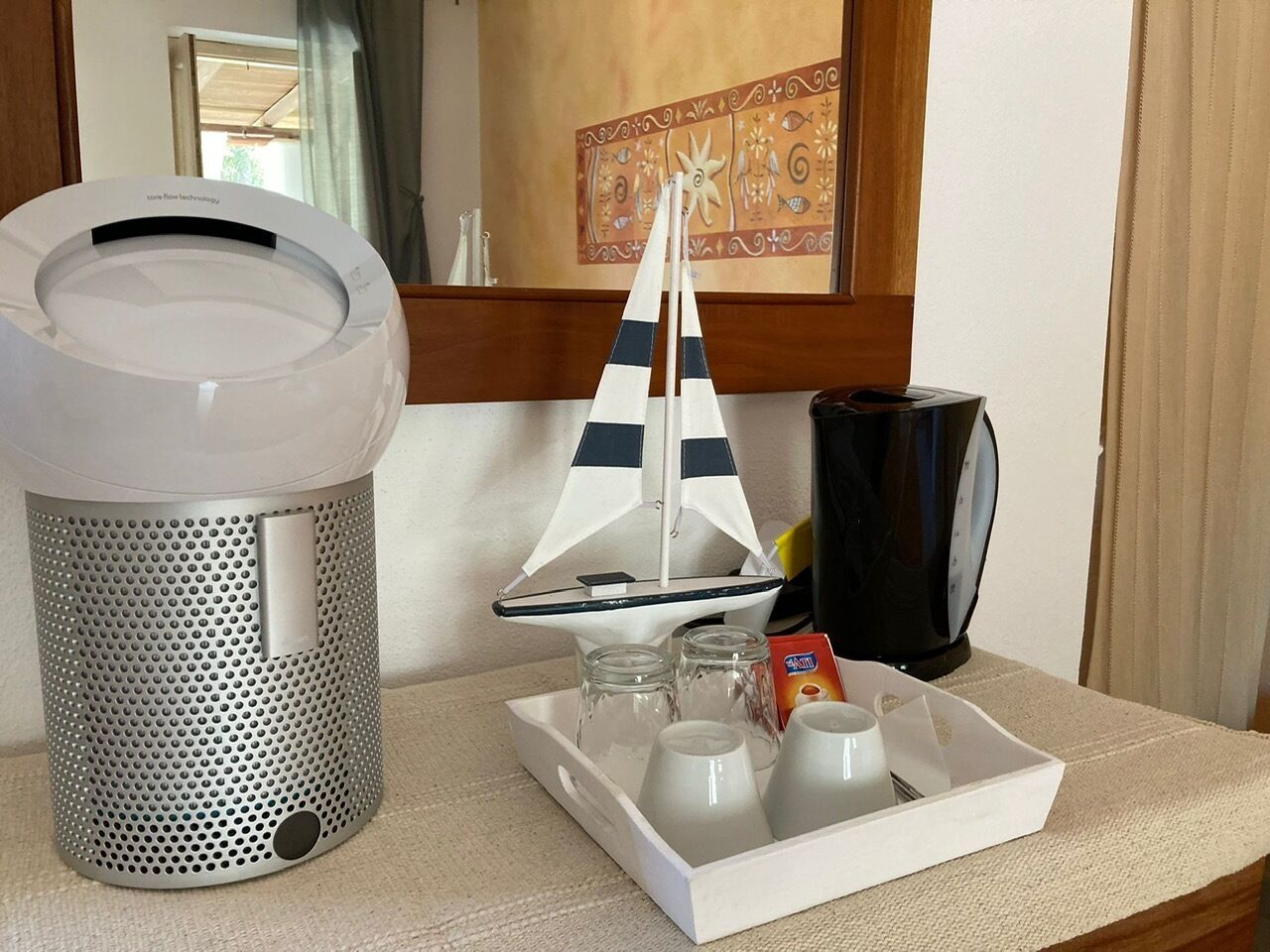 Ein Hotelzimmer mit Kaffeemaschine, Tablett mit Tassen und Beilagen sowie einem dekorativen Modell eines Segelschiffs.