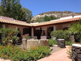 Un patio con techo de tejas, paredes de piedra y una variedad de plantas y flores.