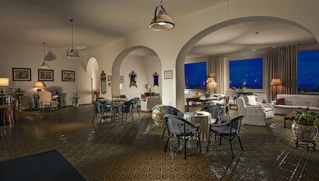 A spacious living room with a dining area, featuring a patterned carpet, arched ceilings, and a large window with a view.. Hotel Bellevue Suite