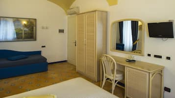 A hotel room with a bed, a blue sofa, a desk with a mirror, a wardrobe, and a television.