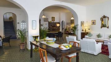 A dining area with a wooden table, chairs, and a buffet setup. There are potted plants and a staircase leading to another room.