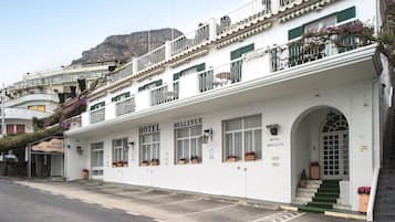 Un hotel blanco con balcones, una escalera y una montaña al fondo.