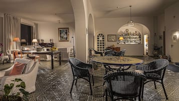 A spacious living room with a dining area, featuring a patterned carpet, wicker furniture, and a bar area with a wine collection.