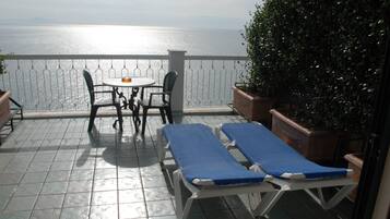 A terrace with a table and chairs, two sun loungers, and a view of the sea.