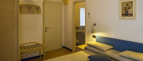 Una habitación de hotel con cama, un banco, una puerta y un aire acondicionado montado en la pared.