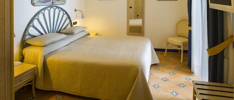 Una cama con cabecera, una silla, una mesita de noche y una lámpara fijada a la pared.