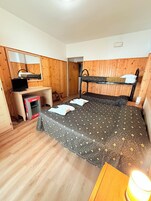 A room with a bunk bed, a desk with a computer, a mirror, and a small table with a lamp.