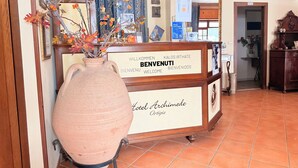 Una reception con una targa di benvenuto in diverse lingue, un grande vaso con fiori e mappe incorniciate alle pareti.
