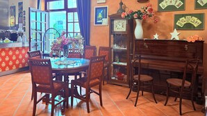 Zona pranzo con un tavolo rotondo, sedie, un pianoforte e un orologio a muro.