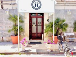 A building entrance with a sign reading "Dal 1980" and a logo above the door. There are potted plants and a bicycle parked outside.