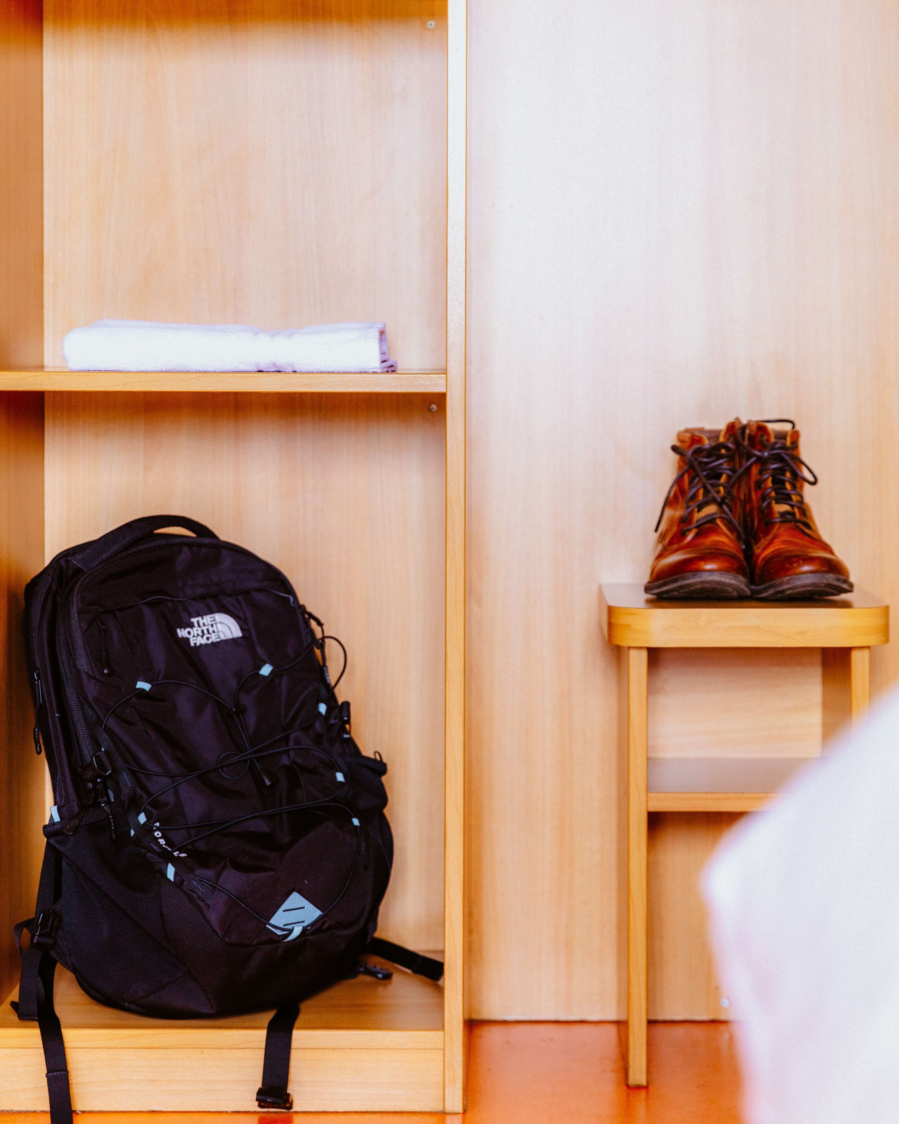 A wooden shelf with a rolled-up white towel and a pair of brown boots on a small wooden table.