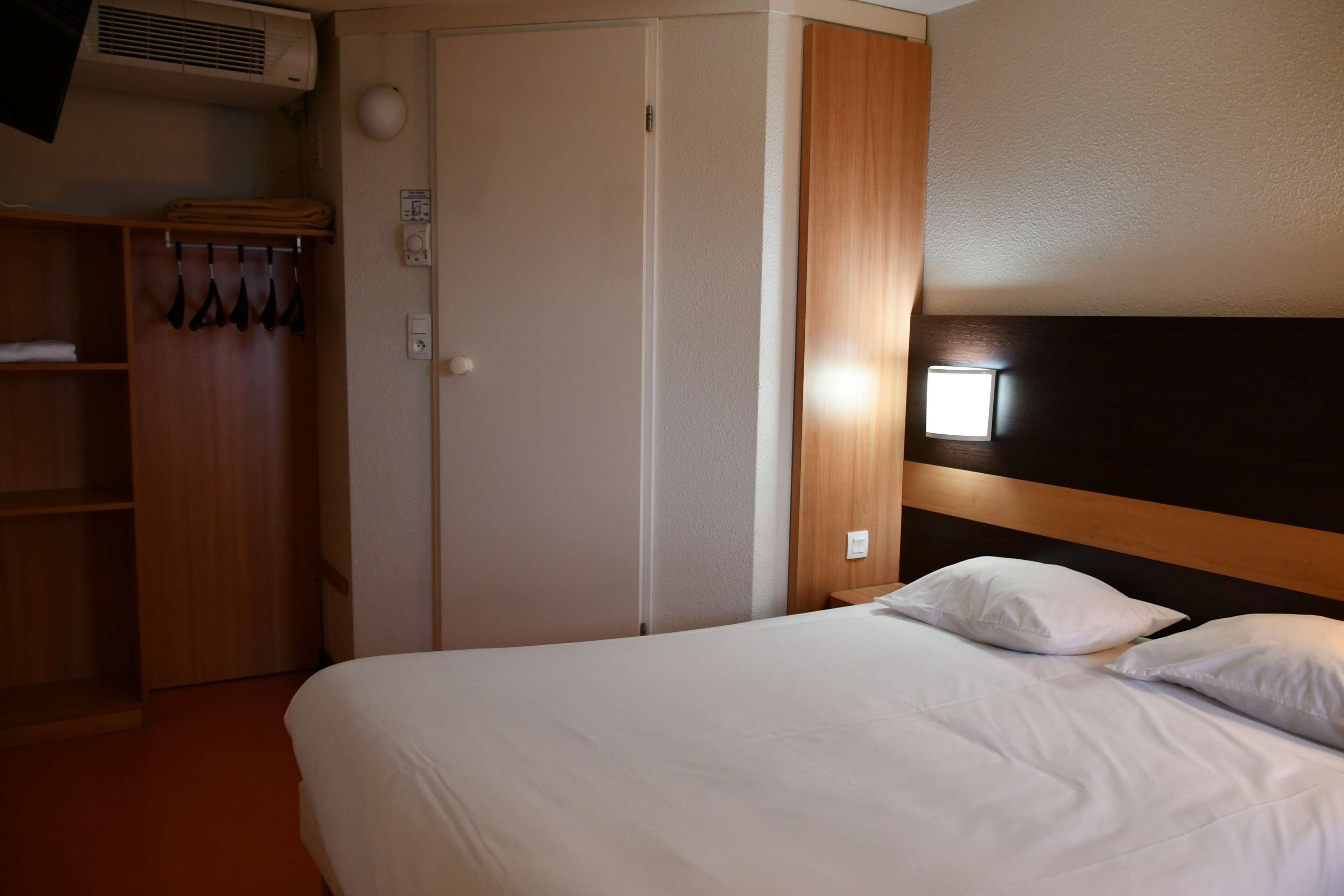 A hotel room with a bed, a wardrobe, and a wall-mounted air conditioner.
