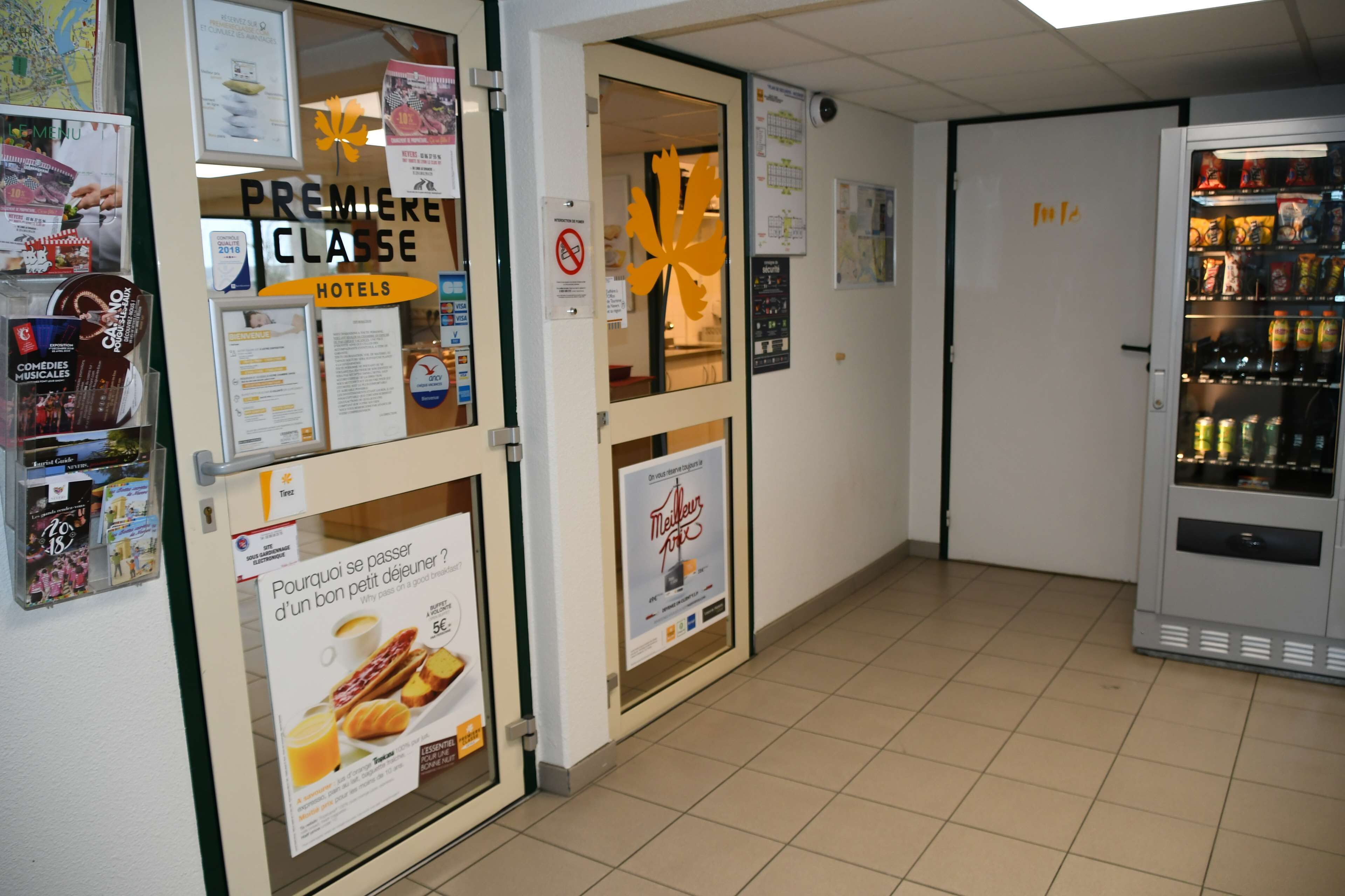 Un couloir d'hôtel avec un distributeur automatique, une enseigne « Première Classe » et divers affiches sur les murs.