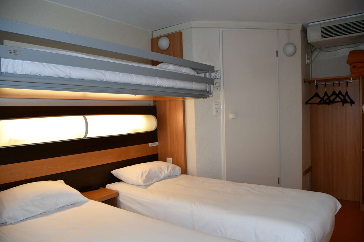 A room with two beds, a bunk bed above, a wardrobe, and an air conditioning unit.