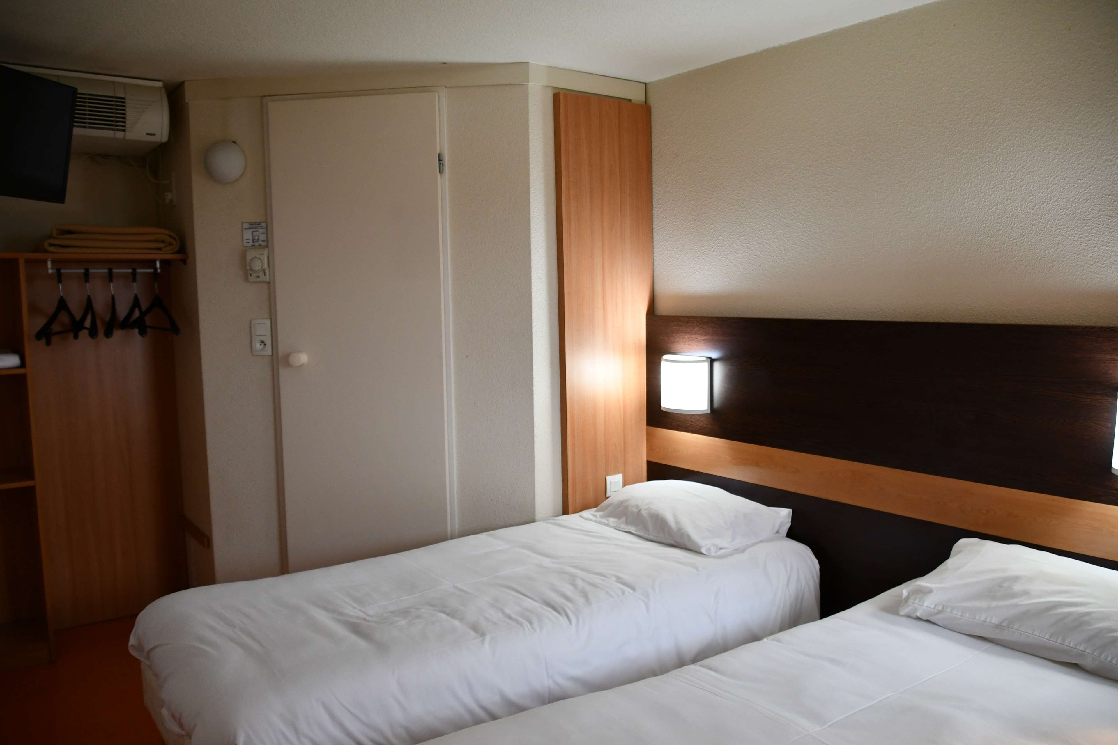 Ein Hotelzimmer mit zwei Betten, einem Holzschrank, einem Kleiderständer und einer Wandklimaanlage.