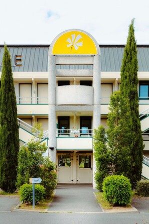 A hotel with a yellow and white logo, a central staircase, and a sign indicating the entrance.