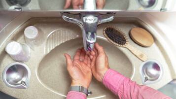 Un lavabo dans la salle de bain, avec un miroir au-dessus, un sèche-mains et une brosse à cheveux posés sur le comptoir.