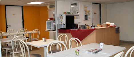 A dining area with tables, chairs, a coffee machine, and a counter with food items.