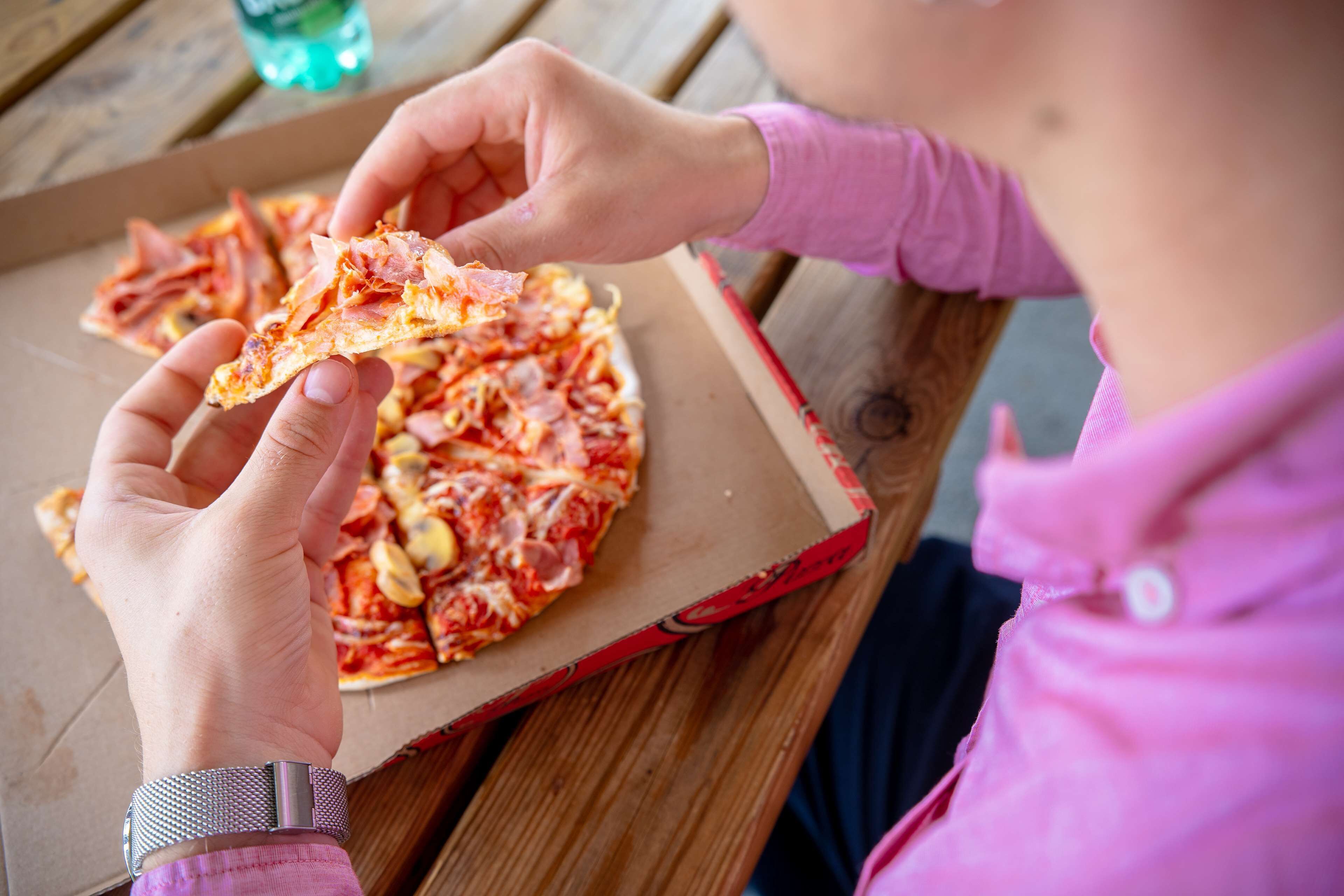 Una persona sosteniendo una porción de pizza de una caja.