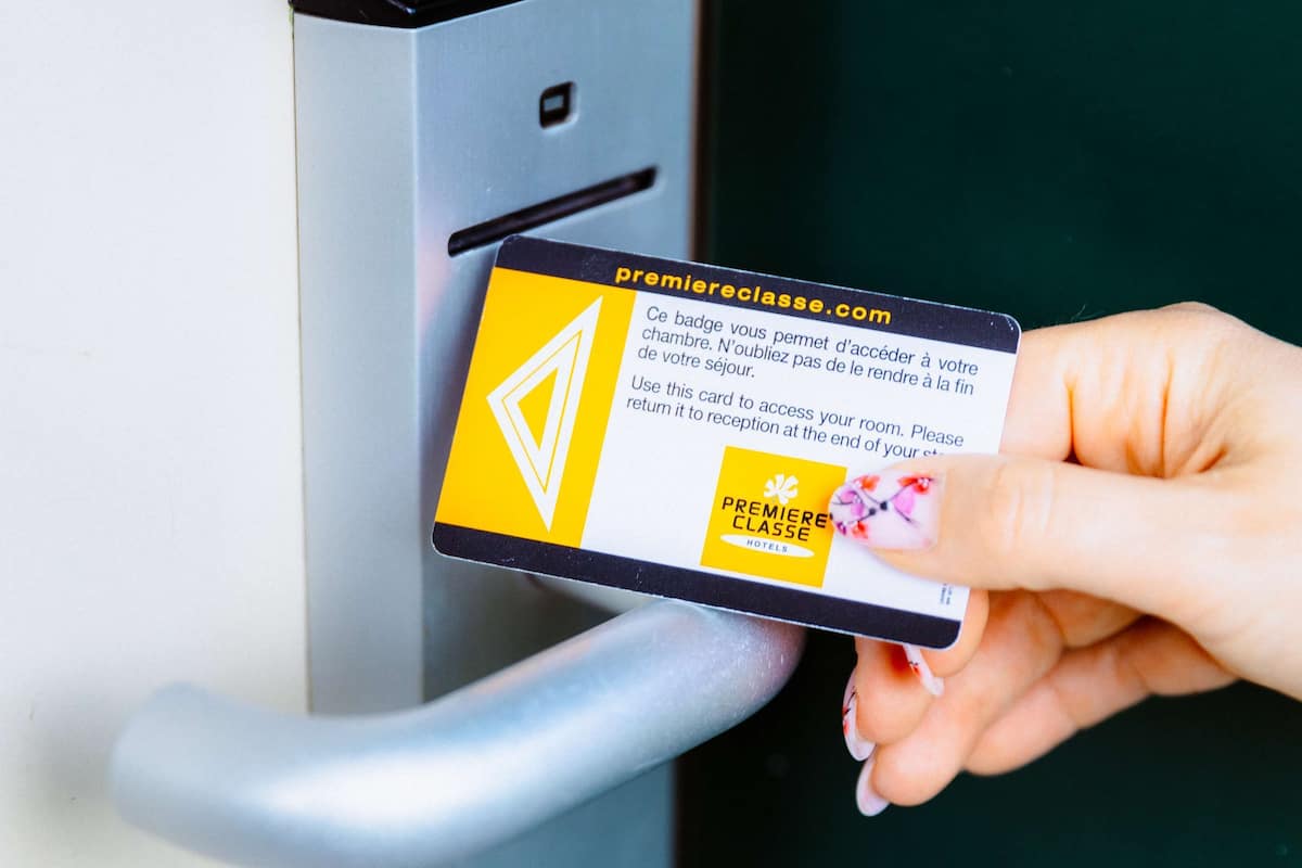 A hand holding a card with a hotel logo and text, inserted into a card reader on a door.