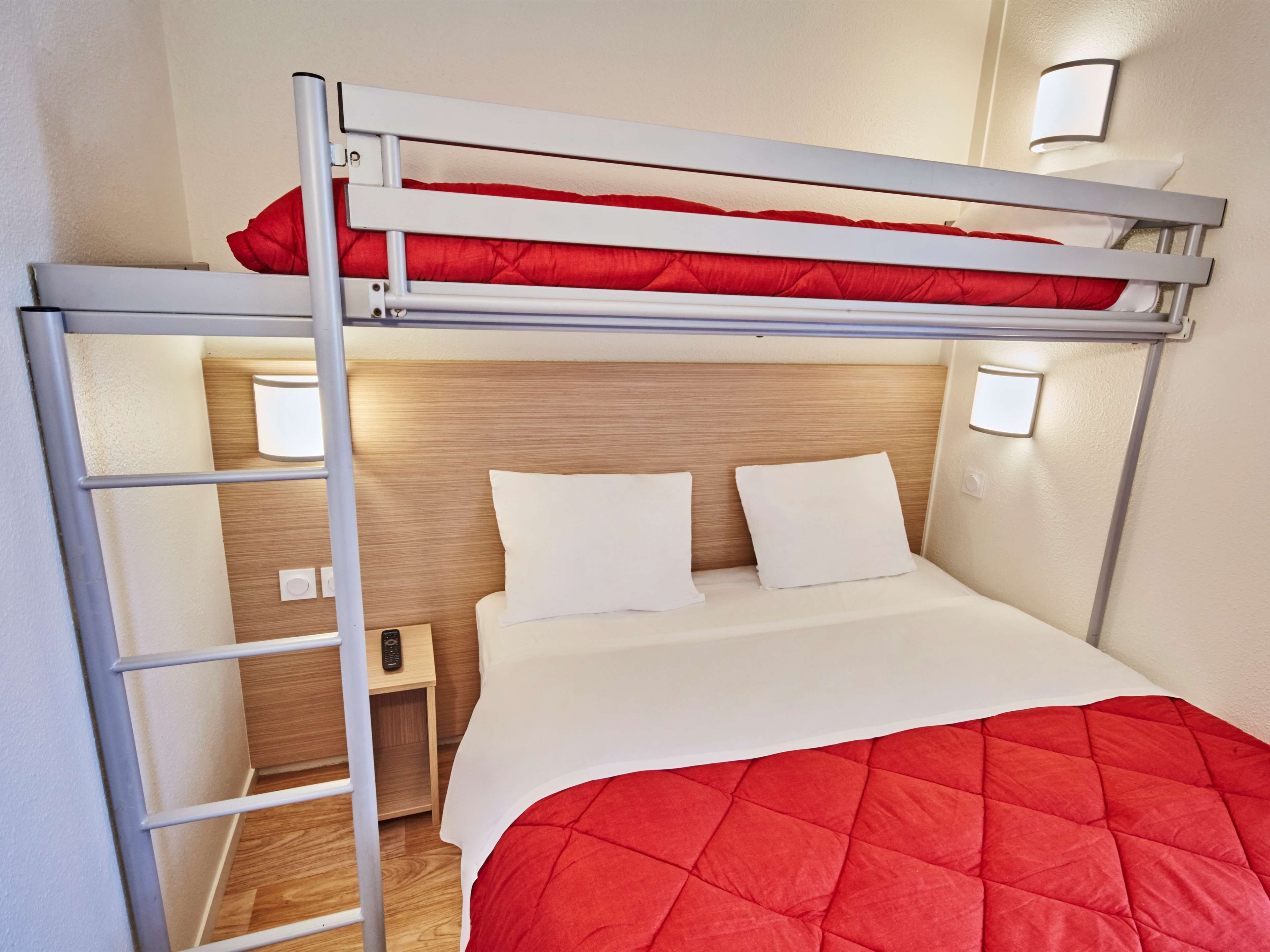 A bunk bed with a red quilted mattress, a wooden headboard, and bedside lamps.