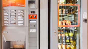 Máquina de vendas com opções de lanches e bebidas, incluindo salgadinhos, biscoitos e refrigerantes como Coca-Cola e Fanta.