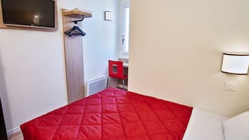 Ein Hotelzimmer mit einem Bett, einem an der Wand befestigten Fernseher, einem roten Sessel, einem kleinen Tisch und einem roten Schrank.