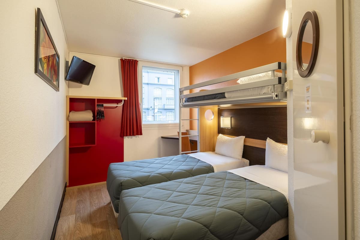 Ein kleines Hotelzimmer mit zwei Betten, einem roten Kleiderschrank, einem Fernseher und einem Fenster mit Vorhängen.
