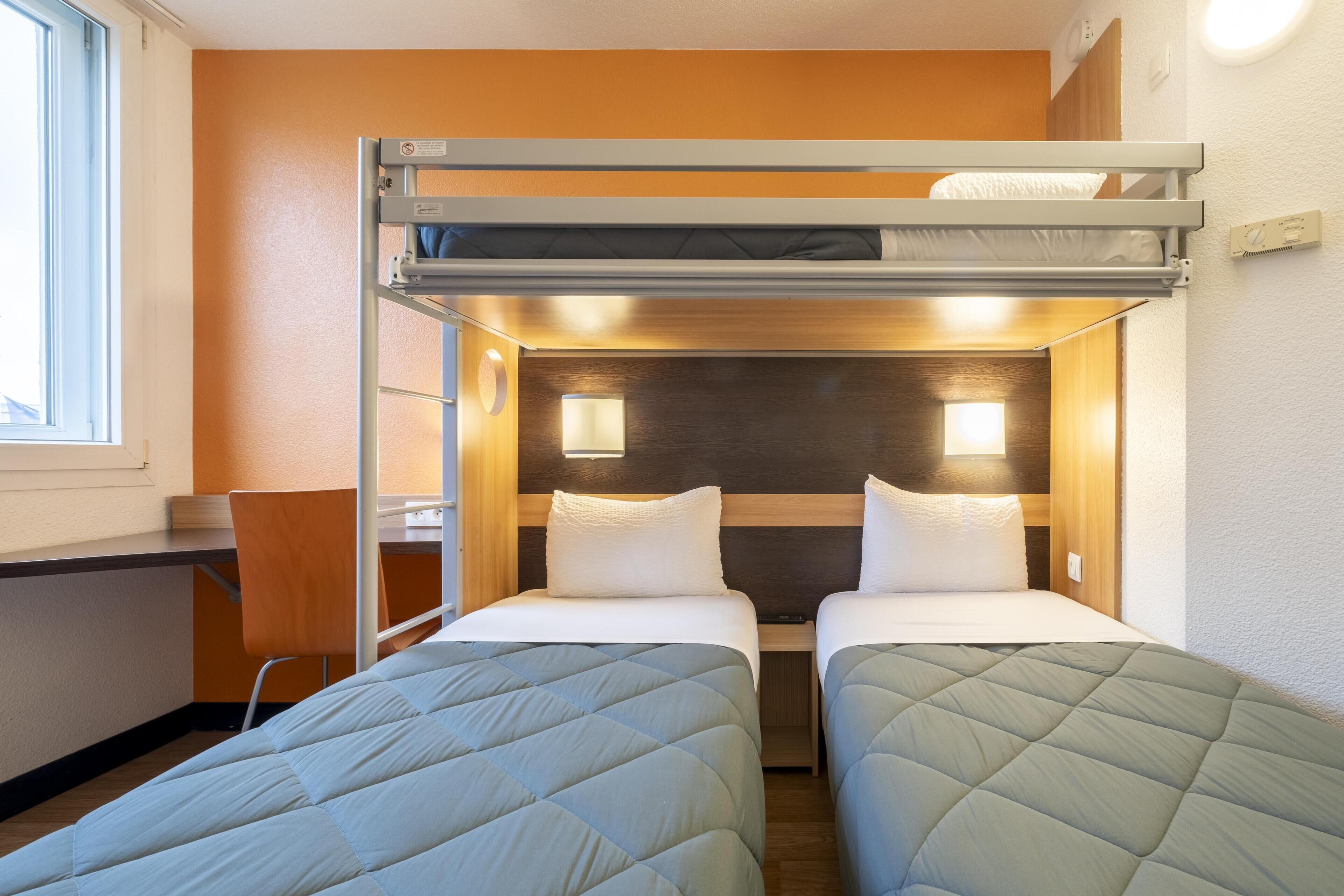 Una habitación de hotel pequeña con dos camas, una litera y un escritorio con una silla.