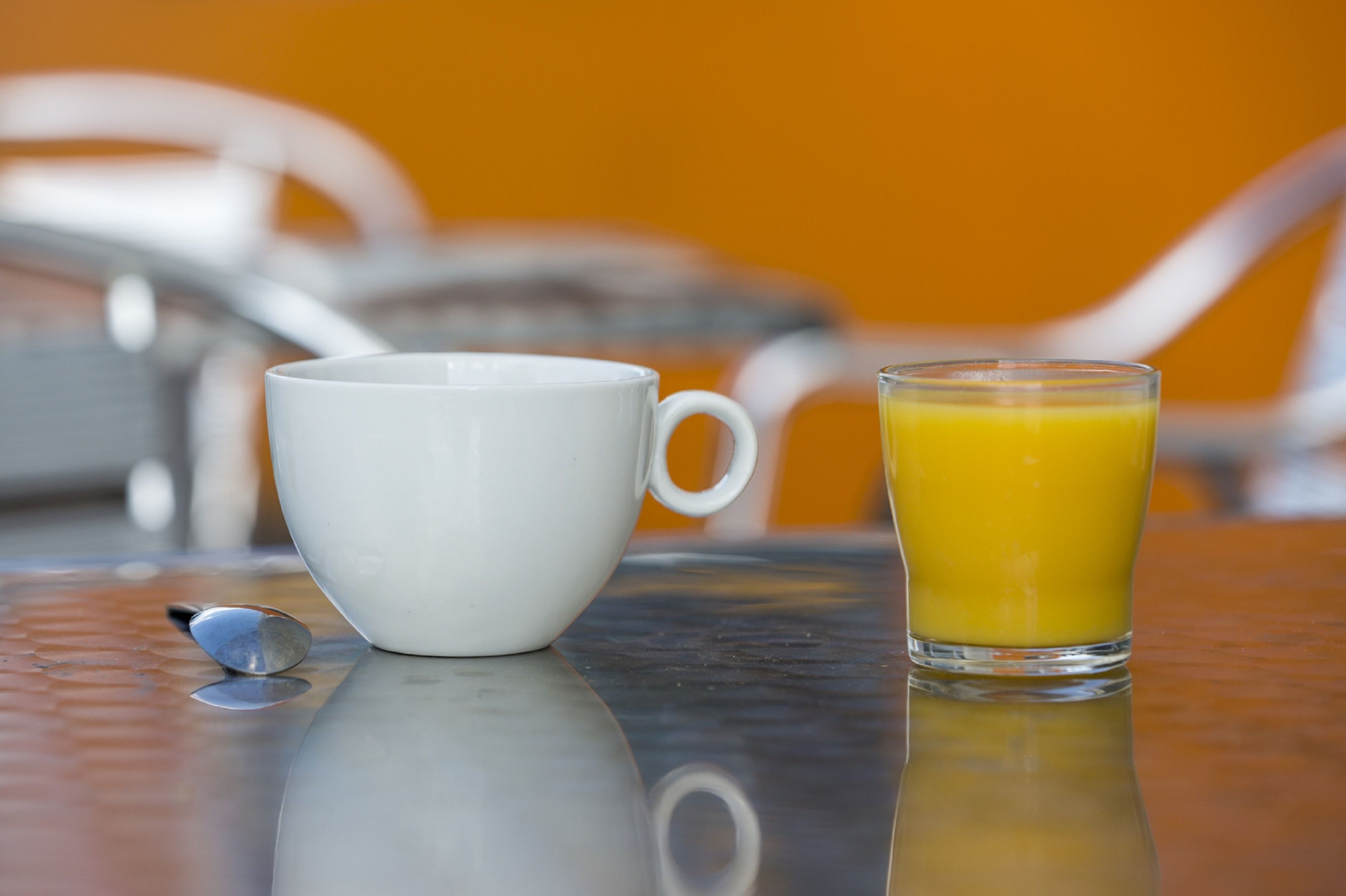 Une tasse blanche et un verre de jus d’orange sur une surface réfléchissante.